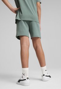 Camiseta de algodón verde con una corte relajado, combinada con pantalones cortos a juego, zapatillas blancas y calcetines blancos con un logo negro.