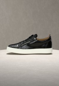 Μαύρο χαμηλό αθλητικό παπούτσι με υφή φιδιού, πλαϊνό φερμουάρ, μαύρα κορδόνια και παχύ λευκό σόλα με ανάγλυφη επιφάνεια σε ουδέτερο φόντο.