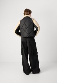 Μαύρο καπιτονέ jacket με κρεμ faux shearling γιακά; το μοντέλο φοράει σκούρες cargo παντελόνες. Οι υφές και τα αντιθετικά υλικά δημιουργούν οπτικό ενδιαφέρον.