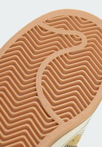 Suela de zapato de goma con un patrón de relieve ondulado, que presenta secciones alternas en zigzag y circulares. El color es un marrón-naranja suave.