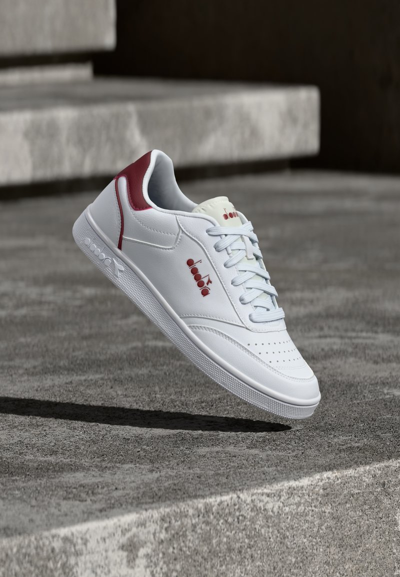 Λευκά δερμάτινα sneakers με υφασμένη ελαστική σόλα, με μπορντό τ όνους στη φτέρνα και ανάγλυφο λογότυπο, καθώς και ανοιχτά μπλε κορδόνια.