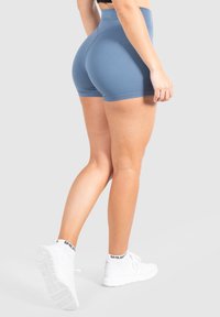 Hoge taille, strakke blauwe shorts van rekbaar materiaal, met een gladde textuur en minimale naden, gecombineerd met witte sneakers.