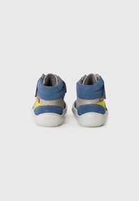 Une paire de petites baskets pour tout-petits bleu, jaune et gris avec des semelles blanches, vue de l'arrière sur un fond blanc uni.