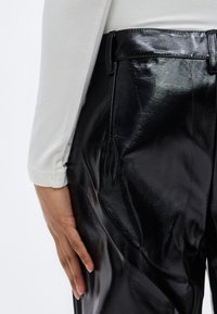 Μαύρο παντελόνι από ψεύτικο δέρμα με γυαλιστερό φινίρισμα, χαρακτηρισμένο από λείο υφή και εφαρμοστή γραμμή, ορατές τσέπες και ανθεκτική μέση.