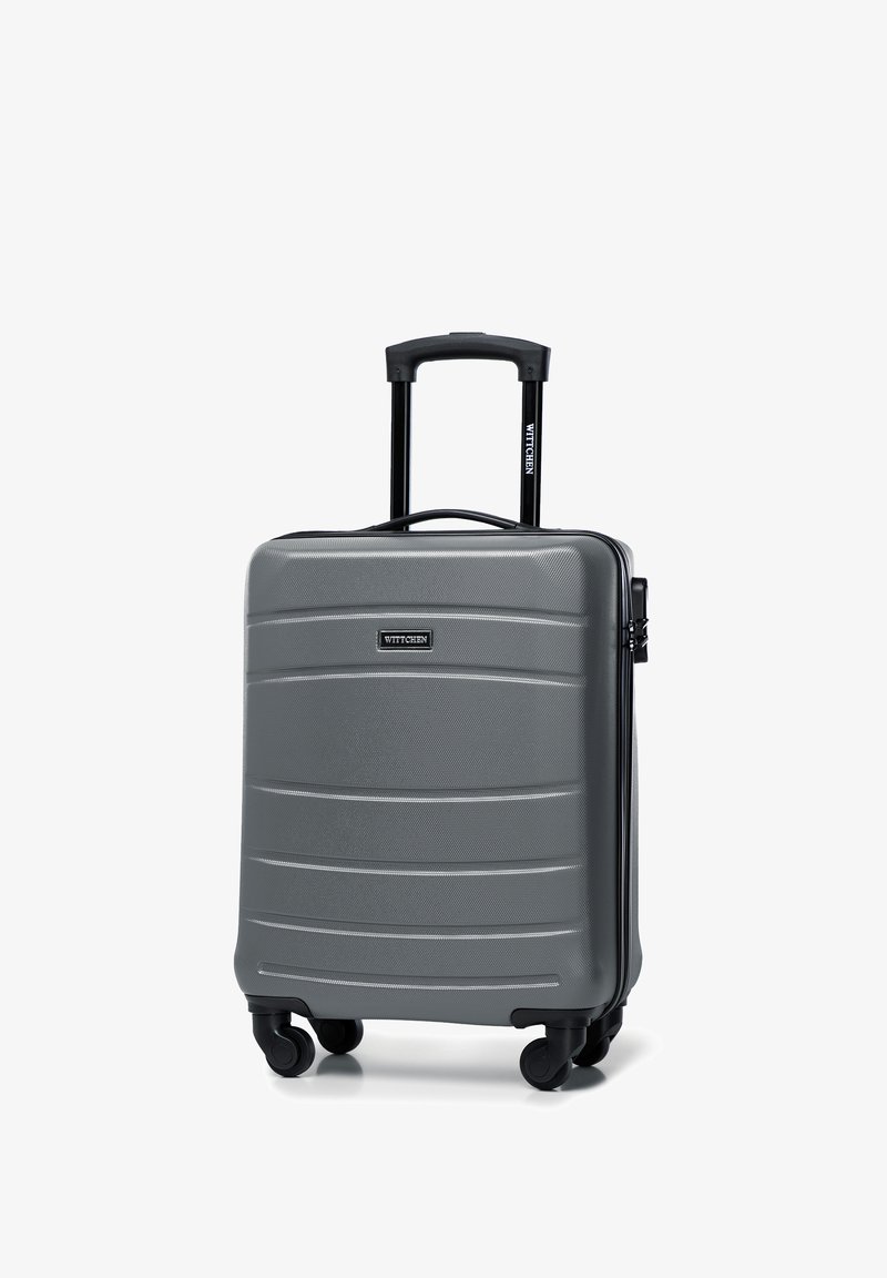 Valigia rigida grigia con strisce testurizzate, un manico telescopico nero e quattro ruote per la mobilità. Presenta un logo del marchio sul fronte.