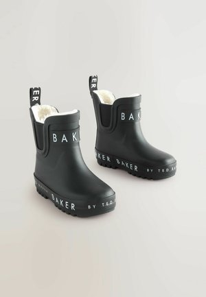 Bottes de cheville en caoutchouc noir avec une semelle texturée, une marque blanche sur les sangles et une doublure intérieure douce et blanche. Deux languettes pour un enfilage facile.