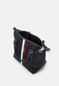 Sac à main en nylon bleu marine avec ferrures dorées, doté d'une fermeture zippée sur le dessus, de deux poignées courtes, et d'une bande blanche et bordeaux sur le devant.