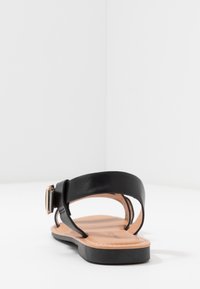 Mustat nahkasandaalit, joissa on tasainen pohja, tyylikkäät remmit ja metallinen solki. Beige sisäpohja viimeistelee ilmeen.