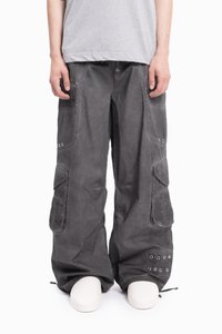 Osoba nosząca luźne ciemnoszare spodnie cargo z wieloma kieszeniami i metalowymi oczkami, w połączeniu z jasnoszarym koszulą i białymi butami.