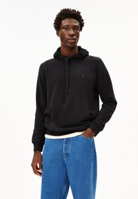 Felpa nera con cappuccio, tasca frontale, cordoncino e un piccolo logo sul petto, abbinata a jeans in denim blu chiaro.