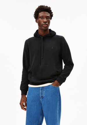 Black hoodie with a front pocket, drawstring hood, and a small logo on the chest, paired with light blue denim jeans.