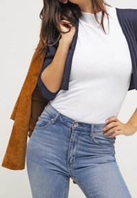 Mörkblå cardigan över en vit åtsittande topp, kombinerad med högmidjade ljusblå jeans. Cardiganen har trekvartsärmar och en mjuk textur.