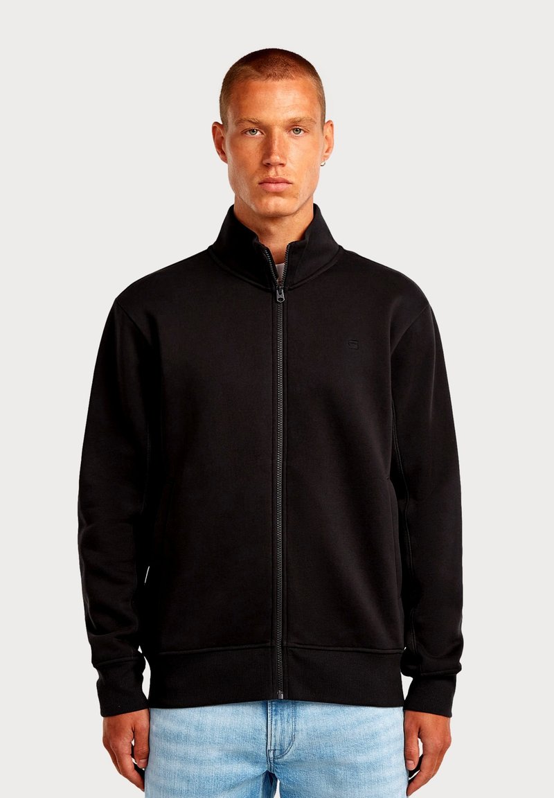 Felpa nera con zip in tessuto morbido, dotata di collo alto, con un logo discreto sul petto e polsini e orlo a costine.