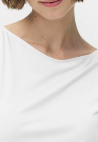 Haut blanc à manches courtes, avec un col large, confectionné dans un tissu lisse et doux, présentant une subtile draperie et des coutures minimales.