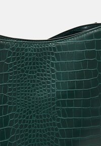 Dark green handbag with a textured, faux crocodile leather finish. Curved top edge and smooth, glossy surface accents.