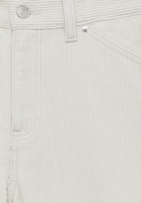 Tissu en velours côtelé blanc avec des côtes verticales, comportant un bouton en métal et des poches cousues. Surface texturée et coutures propres.