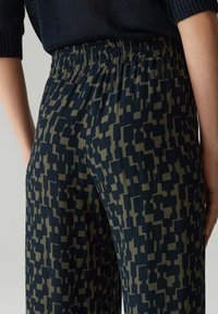 Pantalons à taille élastique avec un motif géométrique en bleu marine foncé et vert olive, présentant un tissu doux avec une coupe fluide et décontractée.
