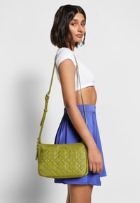 Borsa a tracolla trapuntata verde con finitura liscia, tracolla regolabile e discreti dettagli in oro. Adatta per l'abbigliamento casual.