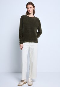 Maglione verde oliva peloso con maniche lunghe, scollatura tonda, abbinato a pantaloni cream a gamba larga e sneaker beige su uno sfondo neutro.