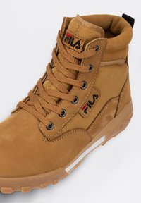 Baskets montantes brunes en cuir et en maille, avec un col rembourré, un design à lacets et un logo Fila sur le côté. Semelle en caoutchouc.