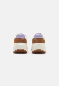 Brązowe zamszowe i białe teksturowane sneakersy z fioletowymi akcentami i logo na pięcie. Posiadają grubą, żebrowaną podeszwę dla dodatkowego wsparcia.
