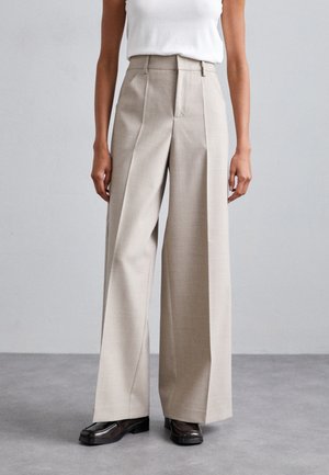 Μπεζ παντελόνια με φαρδιά μπατζάκια, επίπεδο μπροστινό και πλαϊνές πιέτες, φτιαγμένα από ελαφρύ ύφασμα. Συνδυασμένα με σκούρες, γυαλιστερές γόβες.