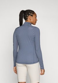 Langärmliges, tailliertes Oberteil in Marineblau mit geometrischem Muster in Pink und Weiß. Hoher Kragen und strukturiertem Stoff, geeignet für aktive Freizeit.