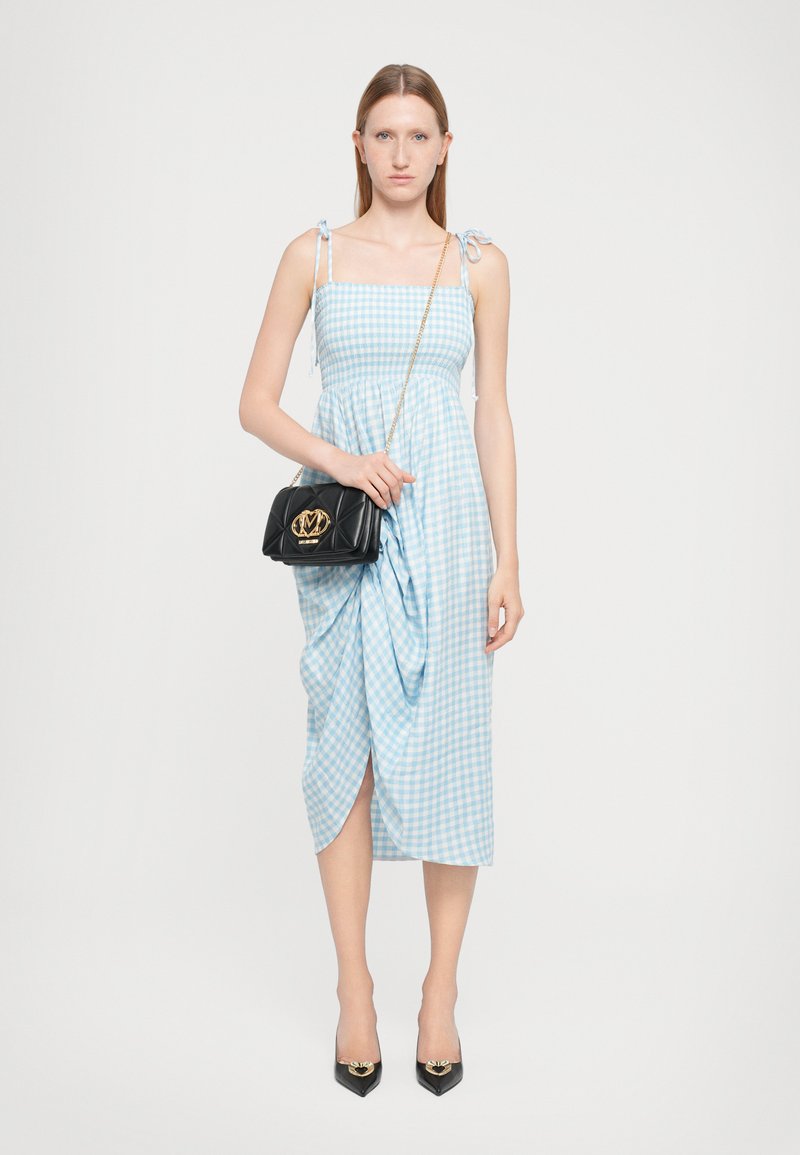 Himbeerblaues Gingham-Midi-Kleid mit Bindeträgern, gerafftem Bund und einem seitlichen Schlitz. Kombiniert mit einer schwarzen gesteppten Handtasche und spitz zulaufenden schwarzen Pumps.