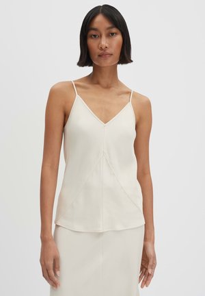 Top sans manches de couleur crème avec un décolleté en V, doté de fines bretelles et d'un design de couture géométrique. Tissu léger avec une texture lisse.