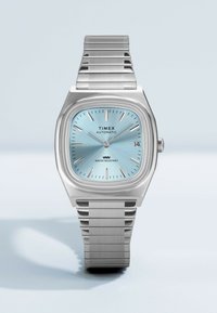 Αυτόματο ρολόι χειρός Timex με ασημένιο μεταλλικό μπρασελέ, ανοιχτό μπλε καντράν, ένδειξη ημερομηνίας και σήμανση αντοχής στο νερό, δείχνει ώρα 10:10:40.