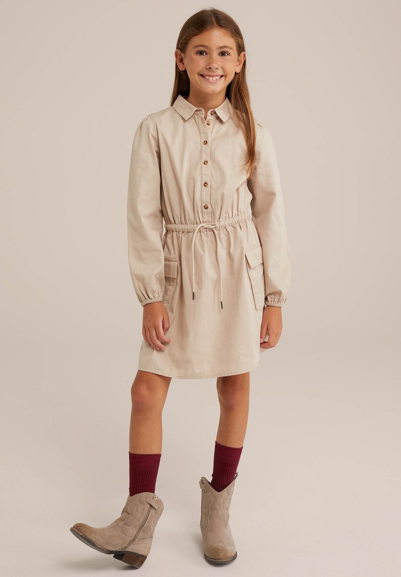 Beez dress, mille nööbiga, elastse piha, pikkade varrukatega ja kahe esi-taskuga. Kanda hallide pahkluudega saapade ja burgundi värvi sokkidega.