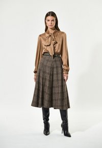 Brun satinbluse med knyttet hals, parret med et ternet nederdel i brune nuancer, med høj talje og sorte stiletto støvler.