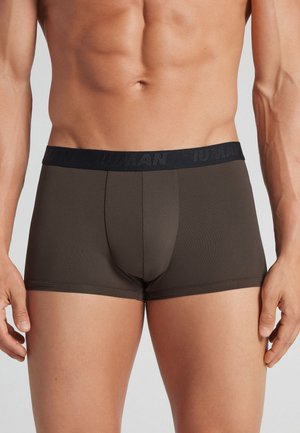 Mandlig overkrop iført mørkebrune tætsiddende boxer shorts med en sort linning, der viser et diskret brandnavn.
