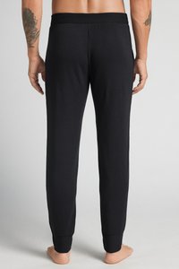 Svarta bomullsloungebyxor har en figursydd design, elastisk midja och avsmalnande mudd. Tyget verkar mjukt och flexibelt.