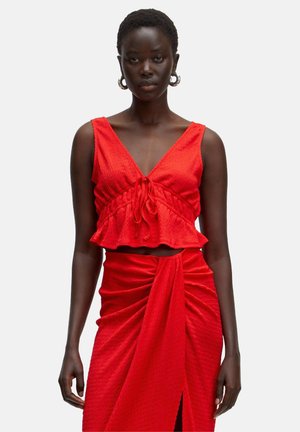 Rode crop top met een V-hals en strikdetail, gecombineerd met een bijpassende rok met gedrapeerd materiaal en een split aan de voorkant. Gestructureerd materiaal.
