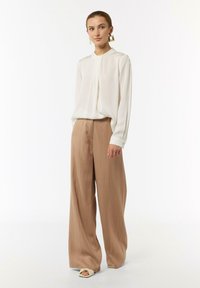 Weiße Bluse mit langen Ärmeln kombiniert mit beigen, weiten Hosen; glatte Stofftextur; minimalistisches Design ohne Muster; flache Schuhe.