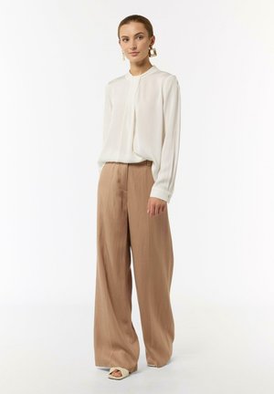 Blusa bianca a maniche lunghe abbinata a pantaloni beige a gamba larga; texture del tessuto liscia; design minimalista senza motivi; scarpe basse.