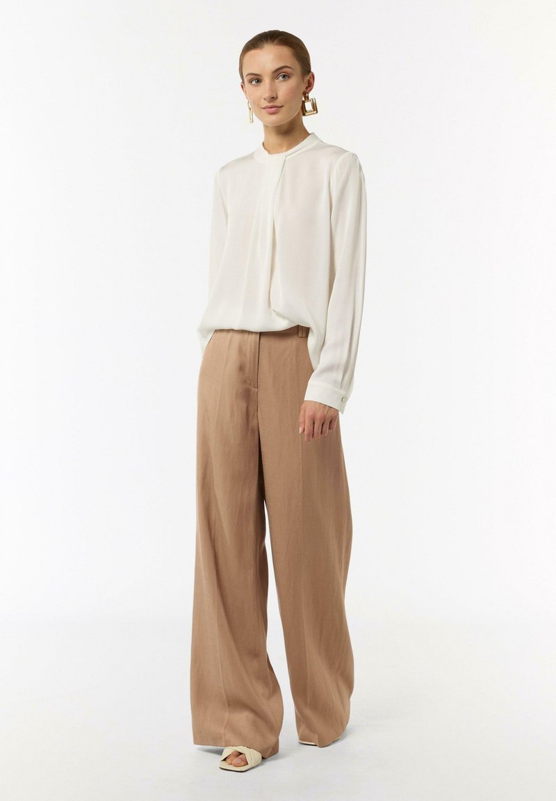 Weiße Bluse mit langen Ärmeln kombiniert mit beigen, weiten Hosen; glatte Stofftextur; minimalistisches Design ohne Muster; flache Schuhe.
