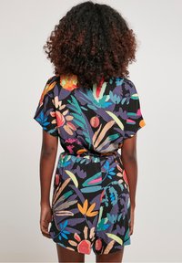 Kortärmad jumpsuit i lätt material med ett livfullt blommönster på svart bakgrund, med en draperad midja och avslappnad passform.