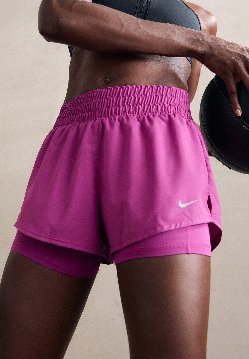 Nike sportovní šortky v jasně růžové barvě, s elastickým pasem a vnitřními šortkami, s malým bílým logem na boku.