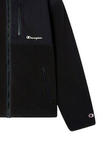 Schwarze Fleecejacke mit einer Reißverschlusstasche auf der Brust und einer Patttasche. Beinhaltet das Champion-Logo in Weiß auf der oberen linken Seite.