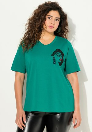 T-shirt verde a V realizzato in cotone, con un design di un volto realizzato con perline nere e colorate sul davanti. Maniche corte, vestibilità rilassata.