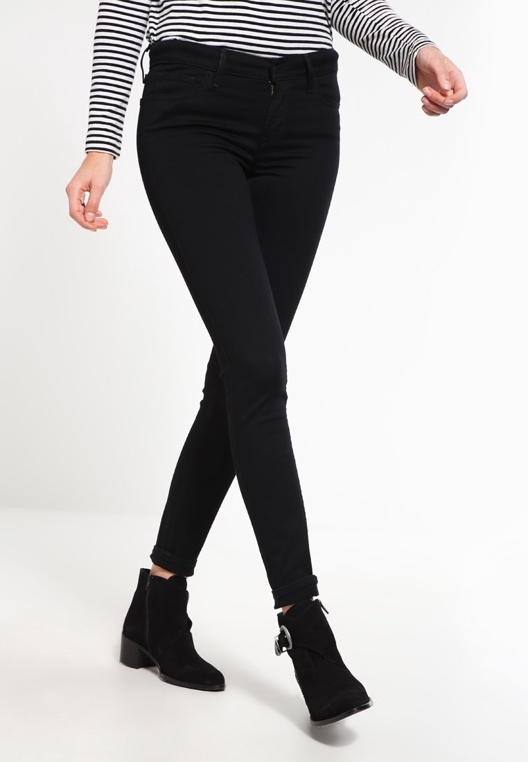 Jean skinny noir à taille haute, avec une texture lisse et des détails de couture subtils. Associé à des bottines noires et un haut rayé.