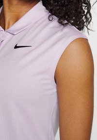 Polo shirt senza maniche di colore lilla con texture a costine, dotato di un logo Nike nero sul petto e di un classico design del colletto.