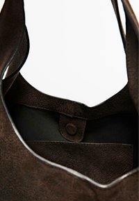 Wnętrze brązowej zamszowej torebki wyściełane czarną tkaniną, wyposażone w magnetyczne zapięcie i gładkie krawędzie.