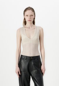 Bež pletena brezrokavnica z globokim V-izrezom, v kombinaciji z črnimi usnjenimi hlačami z okrasnim šivom in gumbi.