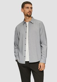 Camicia a quadri blu e bianchi con maniche lunghe, in cotone, e bottoni navy, indossata sopra una maglietta bianca.