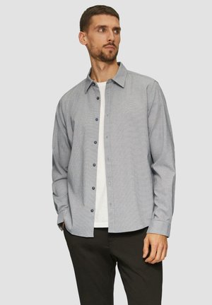 Blauw-wit geruite button-up shirt met lange mouwen, gemaakt van katoen, met marineblauwe knopen, gedragen over een wit t-shirt.