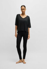 Black V-neck oversized t-shirt paired with black fitted leggings. T-shirt features short sleeves and a slightly curved hem. Smooth texture.