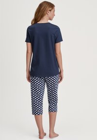 Marineblauw shirt met korte mouwen, gecombineerd met geknipte pyjamabroek met een wit stippenpatroon. Comfortabele, casual pasvorm. Zachte stoftextuur.